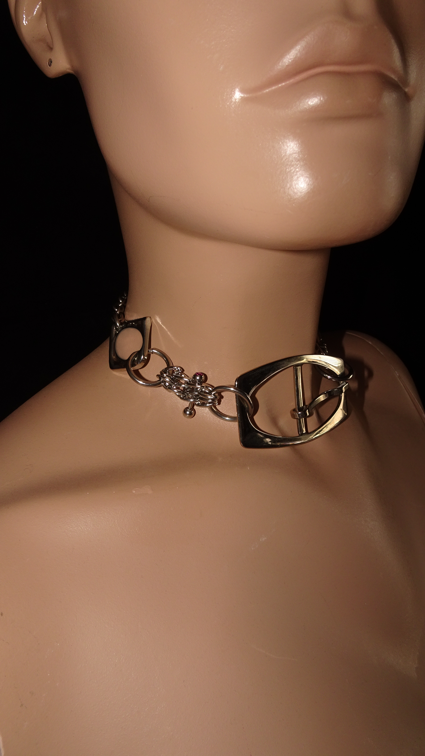 A bold, industrial-inspired upcycled necklace featuring a repurposed equestrian-style buckles, layered chains, a piercing and a pop of pink rhinestones.