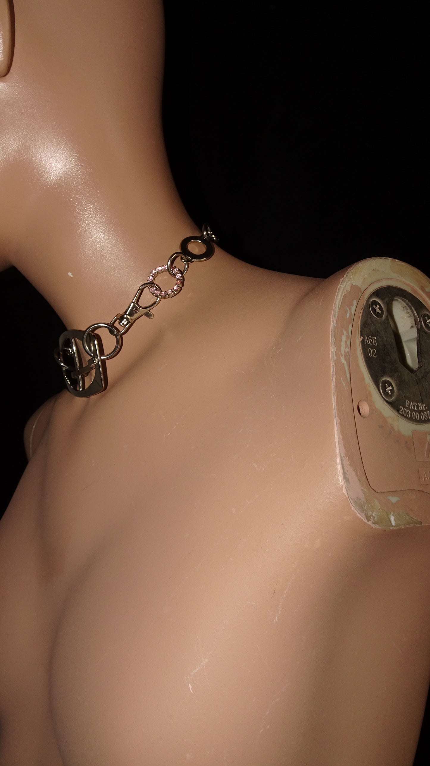 A bold, industrial-inspired upcycled necklace featuring a repurposed equestrian-style buckles, layered chains, a piercing and a pop of pink rhinestones.