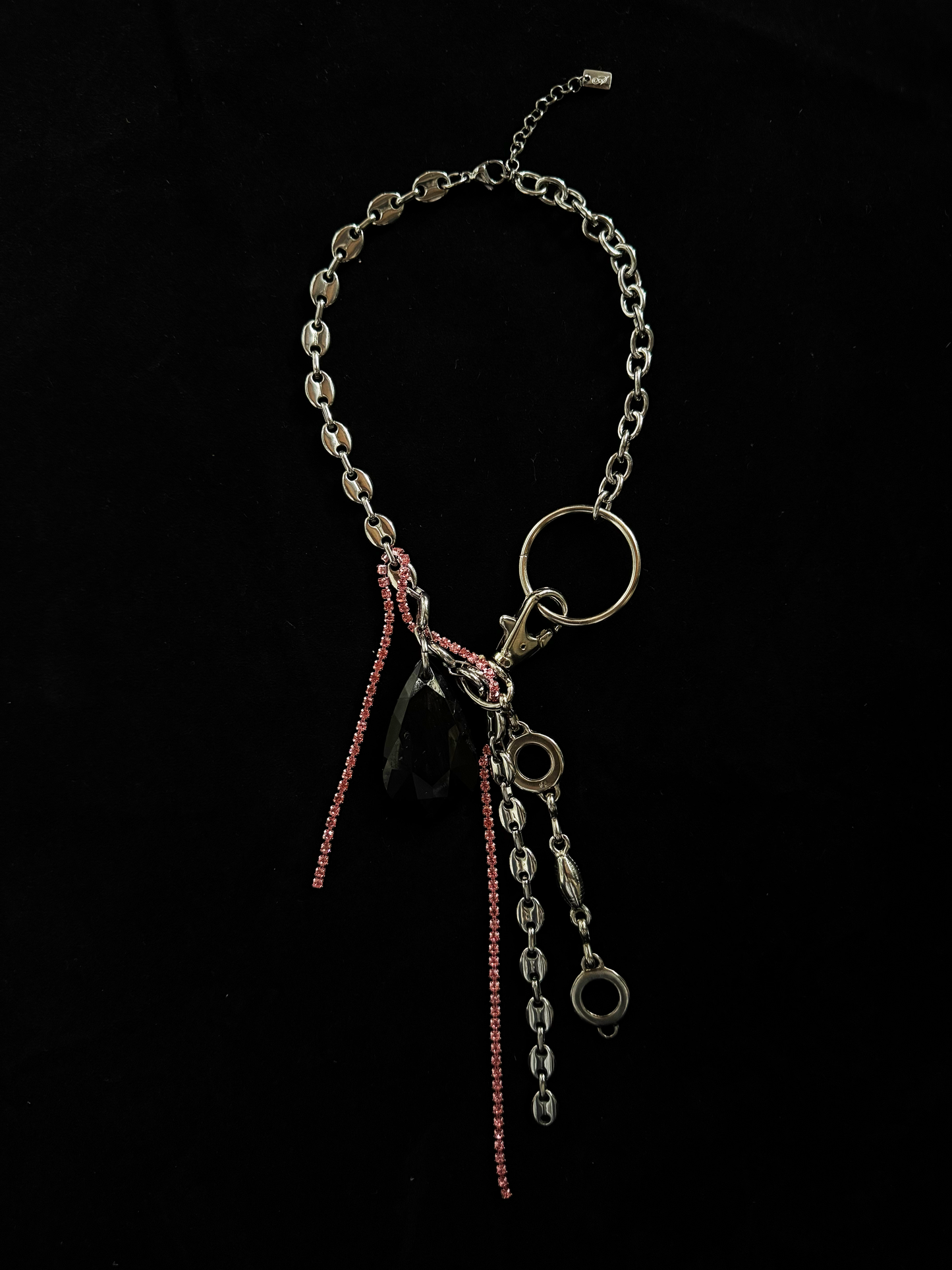 A statement, upcycled necklace by weARCHIVE featuring layered vintage chains, a large black teardrop charm, pink rhinestone strands, and mixed industrial hardware on a bold silver-tone choker or necklace.