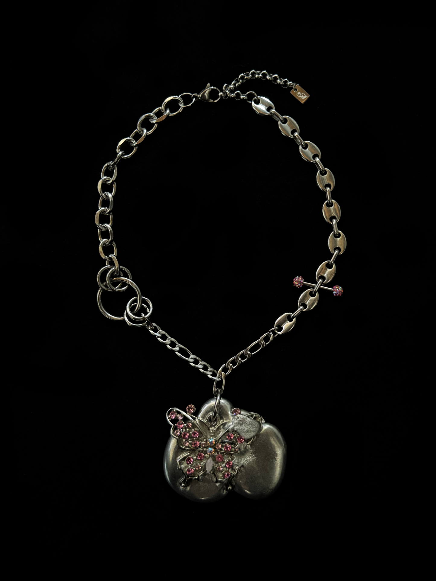 Upcycled asymmetrical necklace with pink rhinestone butterfly on organic silver-tone pendant, vintage chains, and unique piercing detail. Bold, sustainable statement jewelry.