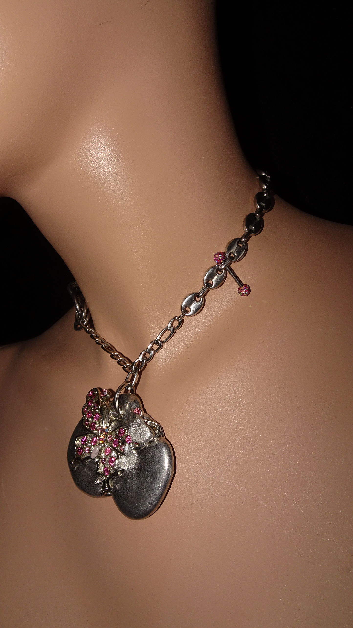 Upcycled asymmetrical necklace with pink rhinestone butterfly on organic silver-tone pendant, vintage chains, and unique piercing detail. Bold, sustainable statement jewelry.