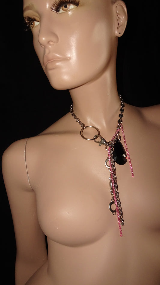 A statement, upcycled necklace by weARCHIVE featuring layered vintage chains, a large black teardrop charm, pink rhinestone strands, and mixed industrial hardware on a bold silver-tone choker or necklace.