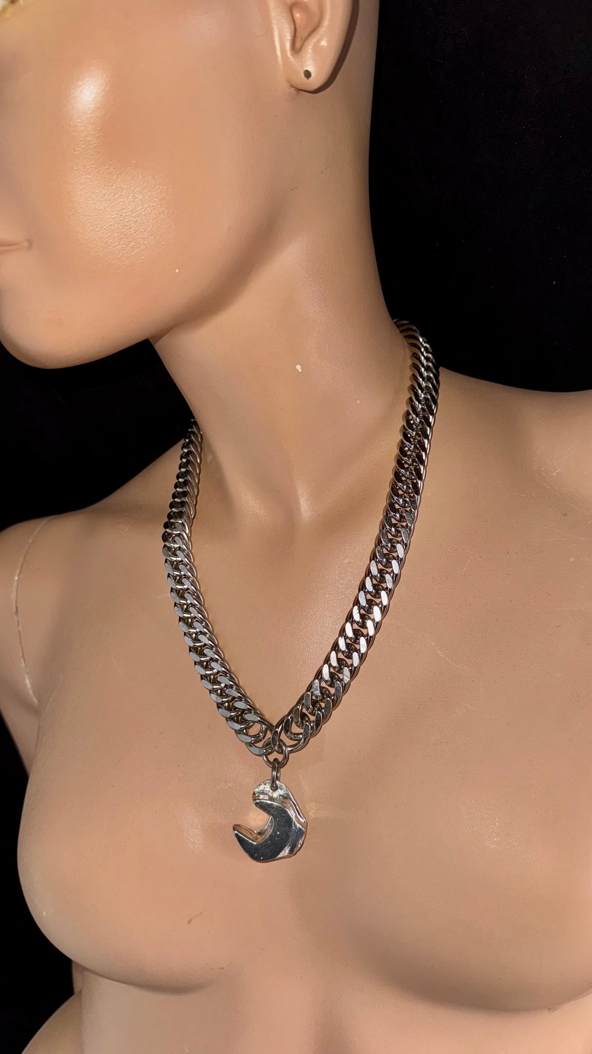 Mannequin wearing a silver chain necklace with a pendant on a black background