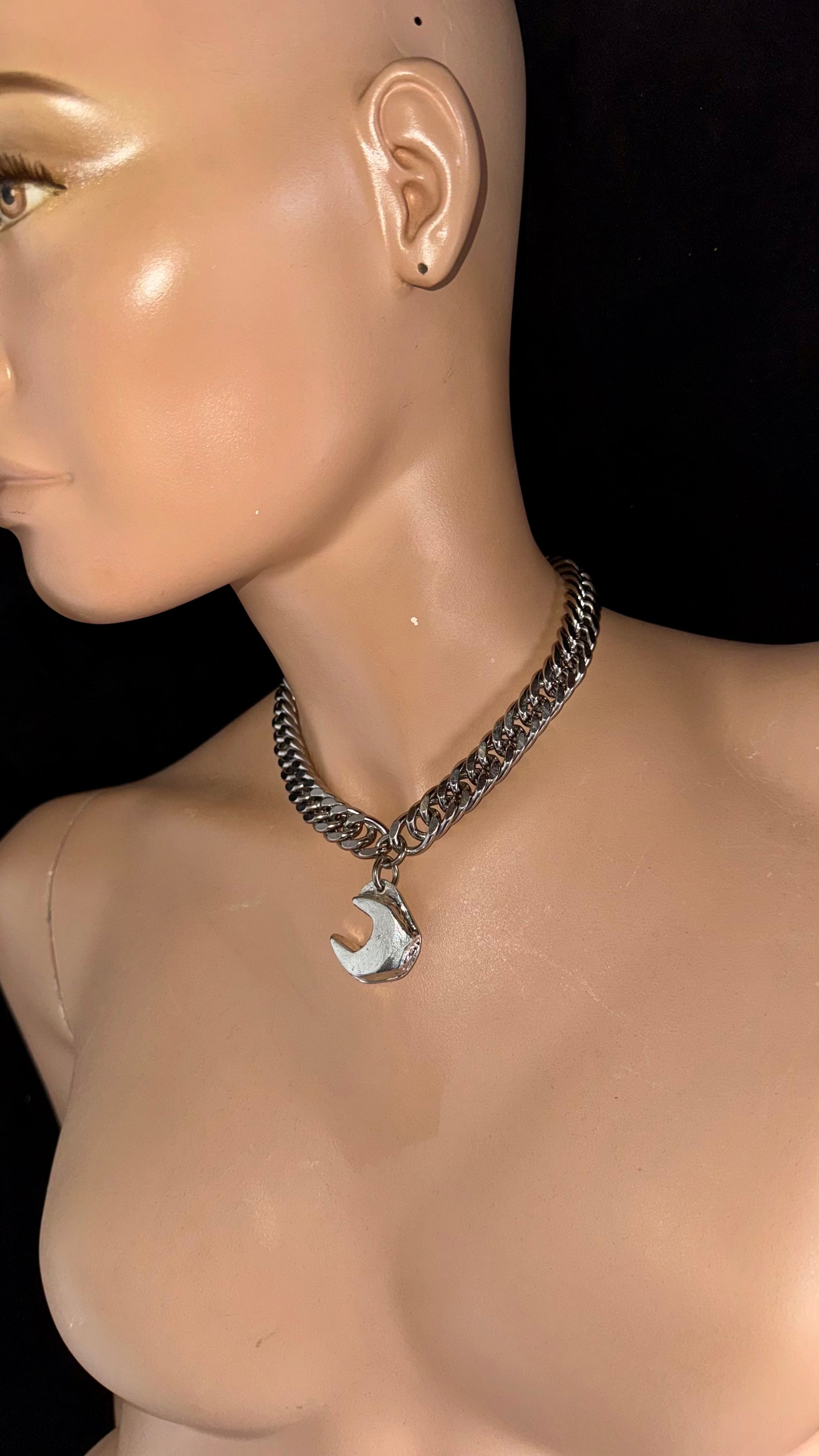 Mannequin wearing a chain necklace with a silver pendant on a black background